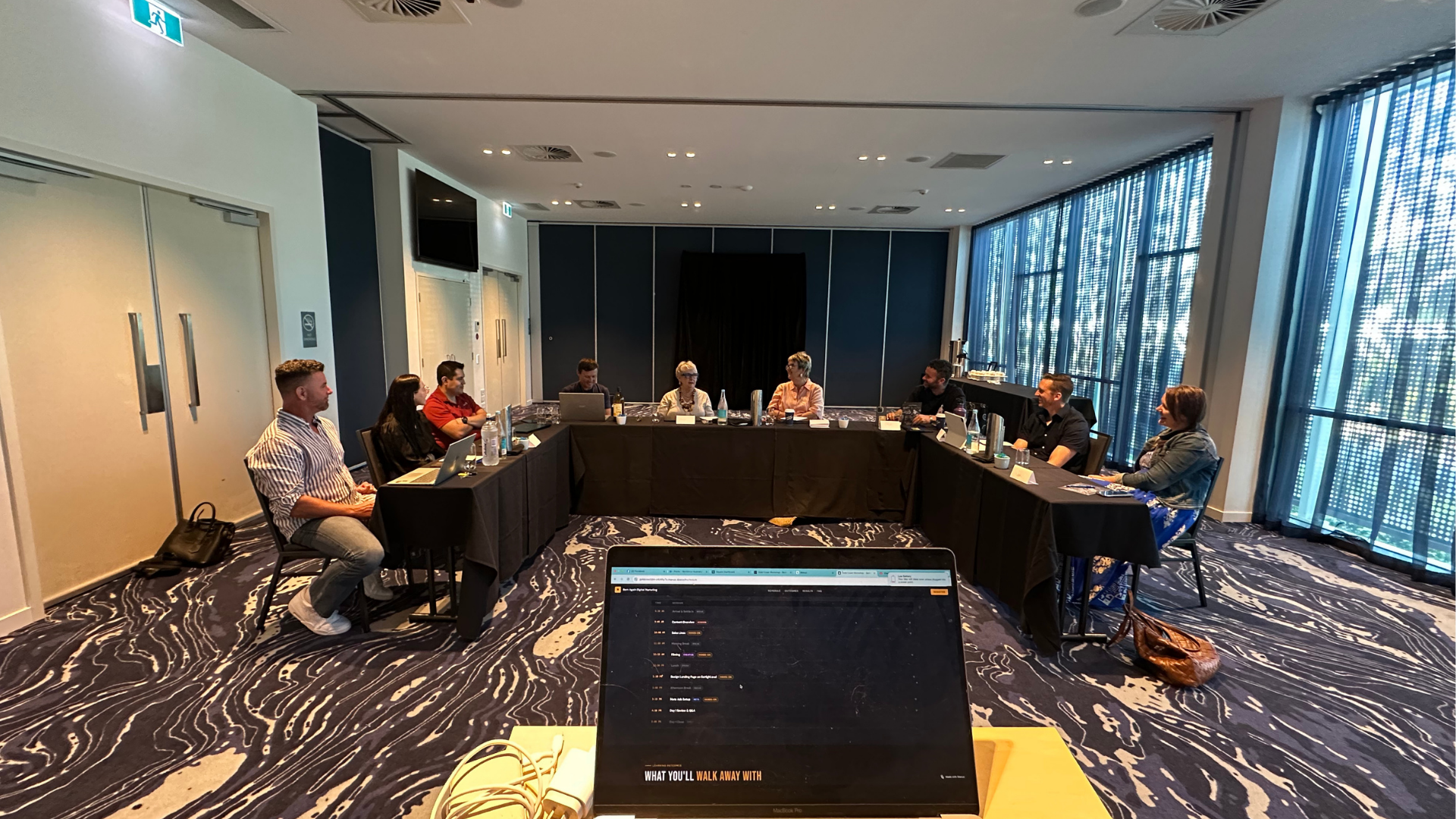 An Ozzie Ai workshop room, laptops open around the table